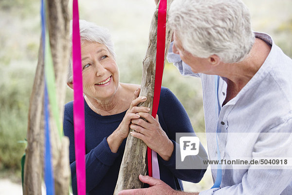 Seniorenpaar steht neben einem geschmückten Baum und lächelt