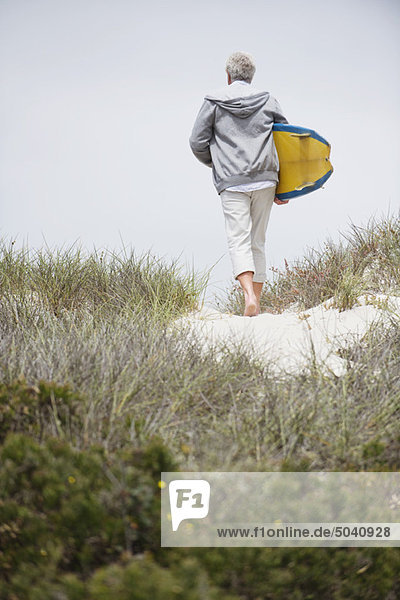 Rear view of a senior man carrying surfboard on the beach