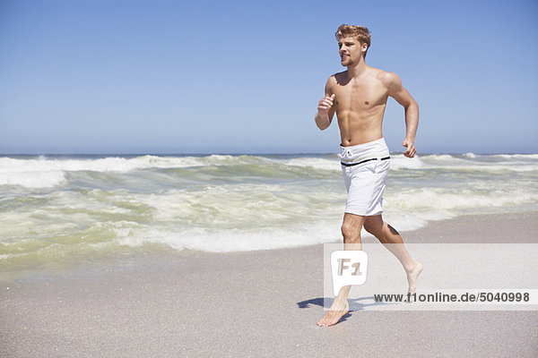 Mann läuft ohne Hemd am Strand