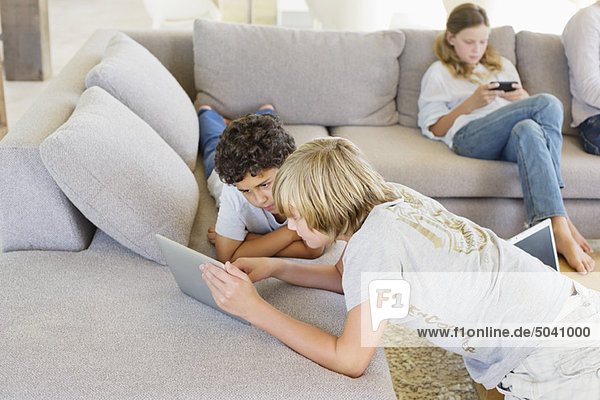 Teenage boy with his brother using a digital tablet and his sister playing video game in the background