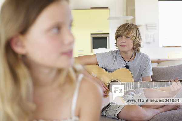 Teenager-Junge spielt Gitarre mit seiner Schwester im Vordergrund