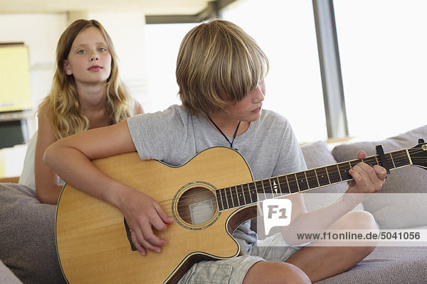 Teenager-Junge spielt Gitarre  ihre Schwester steht hinter ihm und hört zu.