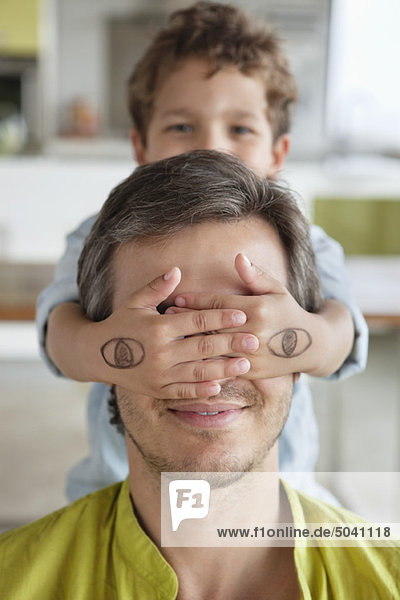 Boy covering his father's eyes