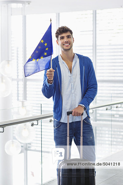 Portrait of a man holding European union flag and a suitcase at an airport