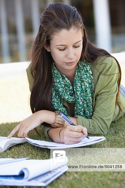Junge Frau auf dem Rasen liegend und auf dem Campus studierend