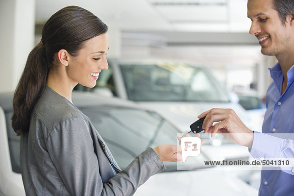 Happy salesperson handing woman car key in showroom