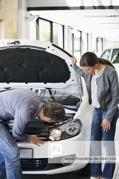 Couple looking at car engine in showroom
