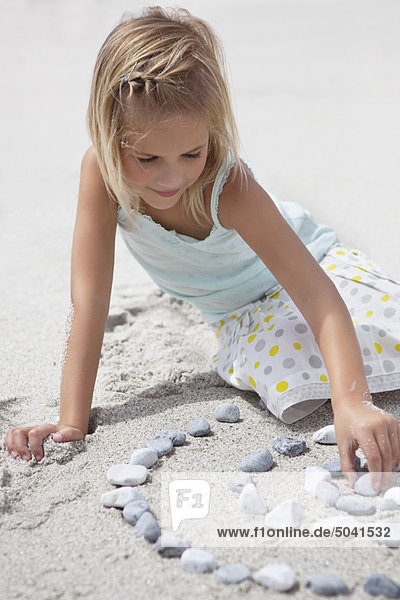 Mädchen spielt mit Kieselsteinen am Strand