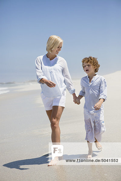 Frau  die mit ihrem Sohn am Strand spazieren geht.