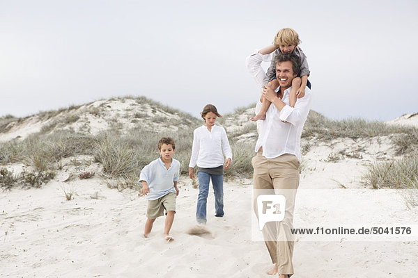 Ein Mann  der mit seinen Kindern auf Sand geht.
