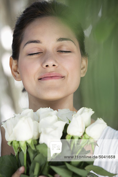 Schöne junge Frau hält einen Strauß weißer Blumen mit geschlossenen Augen.