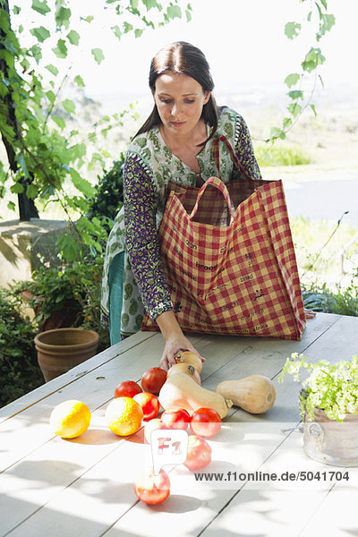 Reife Frau  die Gemüse und Früchte vom Tisch sammelt.