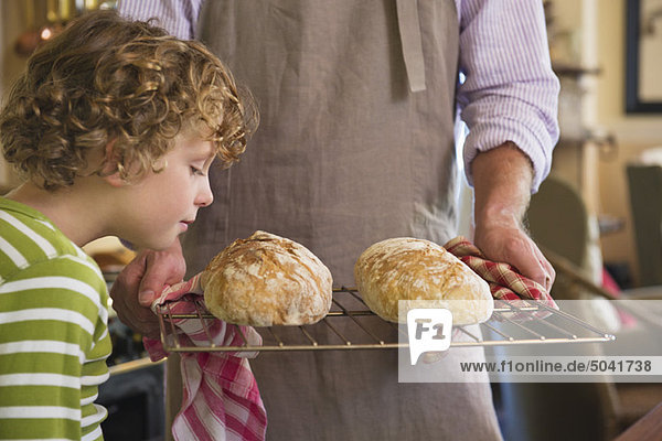 Süßer kleiner Junge  der gebackenes Brot in Vaters Hand riecht.