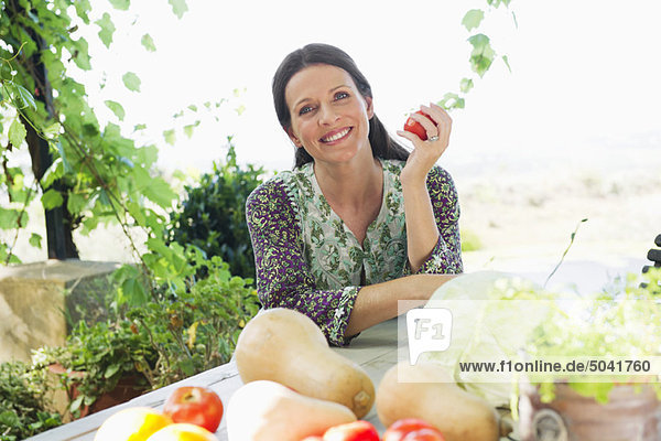 Porträt einer reifen Frau  die mit Gemüse auf dem Tisch sitzt.