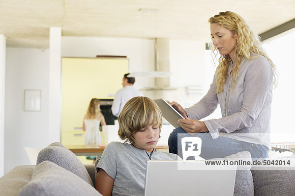 Teenager-Junge mit einem Laptop und seine Mutter mit einem digitalen Tablett