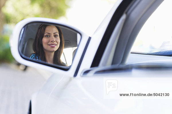 Spiegelung einer lächelnden jungen Frau auf einem Autospiegel