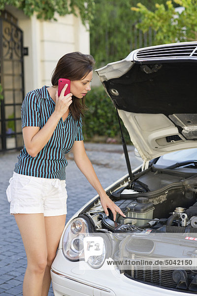 Young woman talking over phone and standing by the broken car