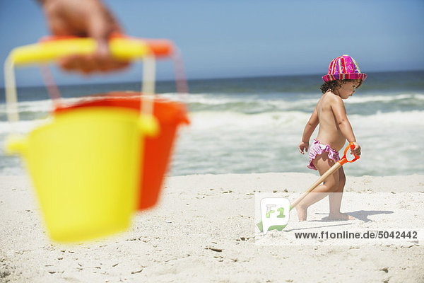 Seitenprofil eines Mädchens  das mit einer Sandschaufel am Strand spazieren geht.