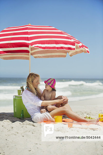 Frau mit ihrer Tochter am Strand sitzend