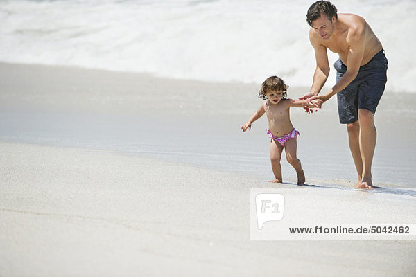 Vater geht mit kleinem Mädchen am Strand spazieren