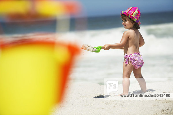 Seitenprofil eines Mädchens beim Graben mit einer Sandschaufel am Strand