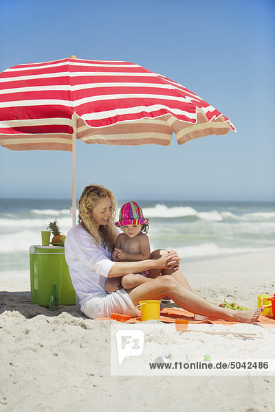 Frau mit ihrer Tochter am Strand sitzend