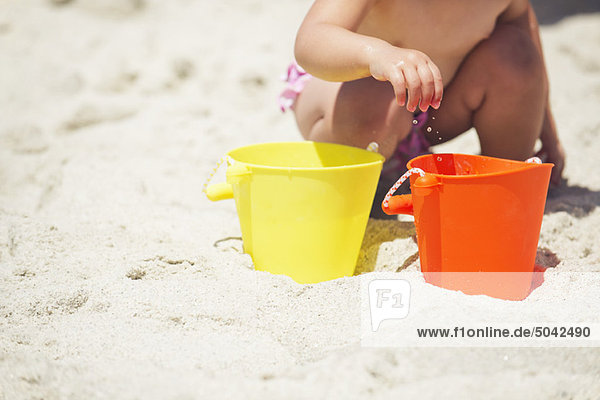 Flachschnittansicht eines Mädchens beim Spielen mit Sand am Strand