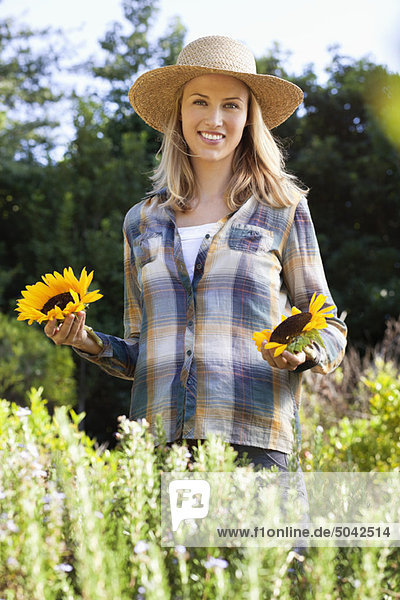 Portrait of a young woman holding sunflowers in a field