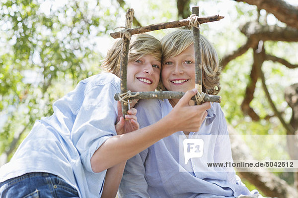 Portrait of children looking through frame of driftwood outdoors
