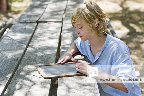 Side profile of a little boy writing on slate outdoors