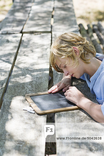Side profile of a little boy writing on slate outdoors