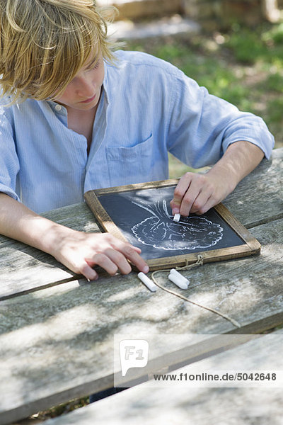 Little boy making drawing of tree on slate outdoors