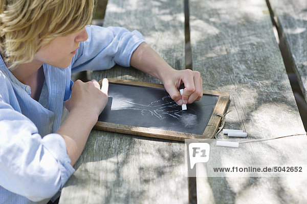Side profile of a little boy drawing on slate outdoors