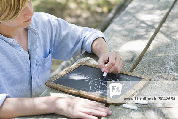 Side profile of a little boy making drawing of tree on slate outdoors