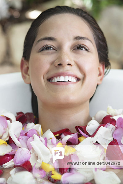 Schöne junge Frau entspannt in der Badewanne mit Blütenblättern