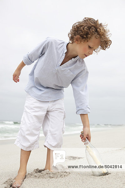 Boy reaching for message in a bottle on beach