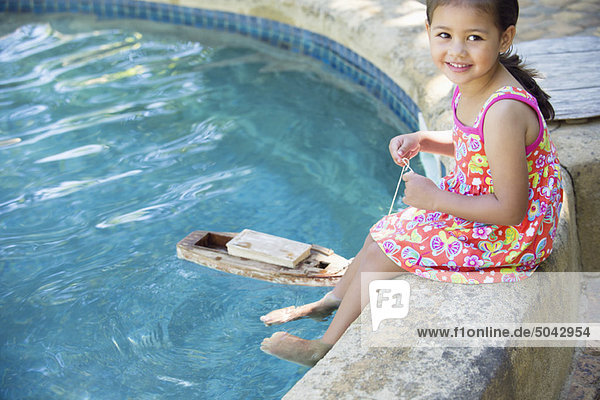 Mädchen sitzend am Rand des Schwimmbades mit Spielzeugboot im Wasser