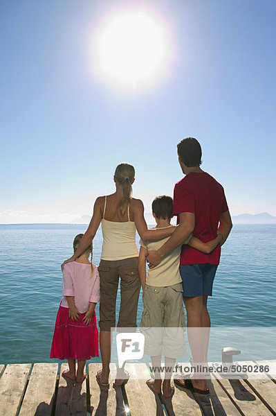 Rear view of family standing on jetty with sun shining