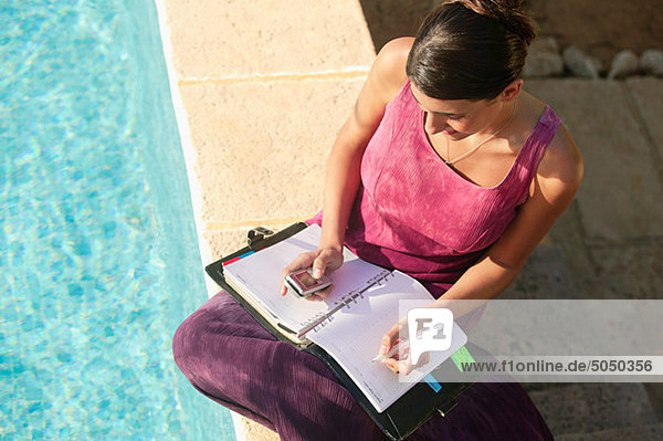 Woman by swimming pool with cellphone and organizer