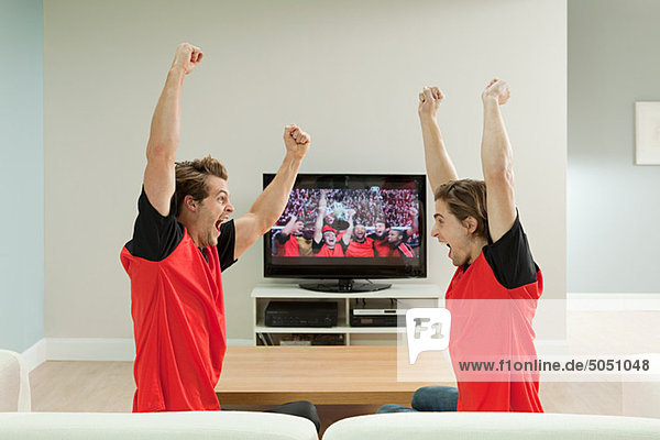 Zwei junge Männer in Fußballshirts beim Fußball schauen im Fernsehen