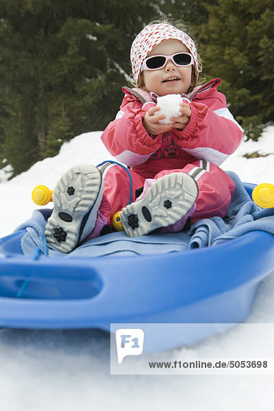 Kleinkind Mädchen auf Schlitten  Schneeball in den Händen