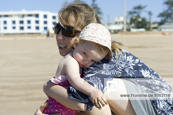 Mutter umarmt kleine Tochter am Strand