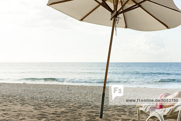 Sonnenschirm am Strand  halbnackte Person auf Liegestuhl liegend
