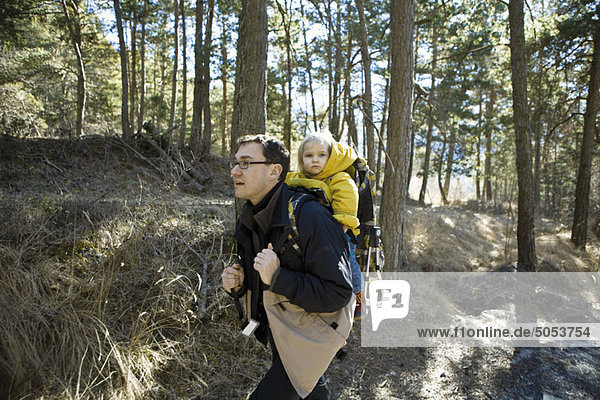Vater Wandern im Wald mit Tochter im Rucksackträger