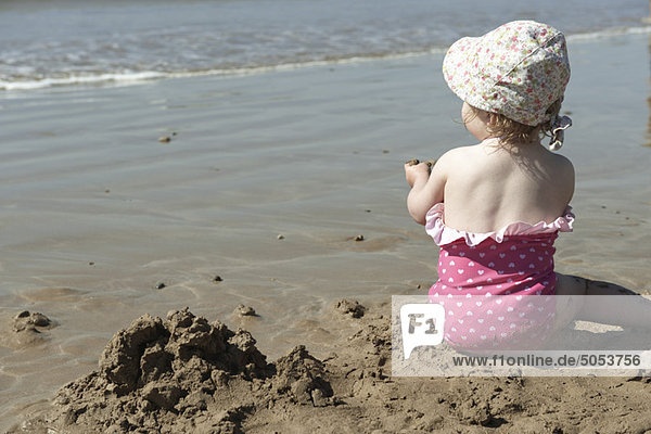 Kleinkind spielt im Sand am Strand  Rückansicht
