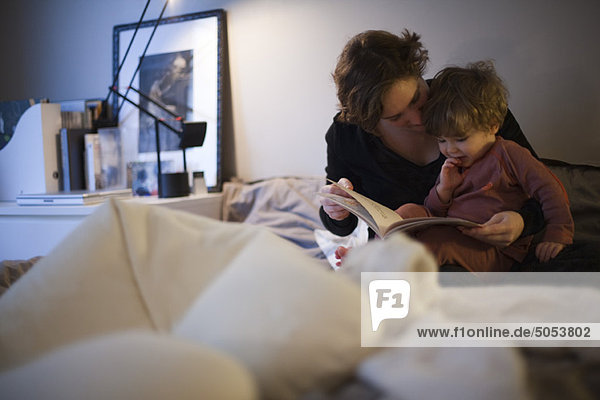 Mutter hält Kleinkind-Sohn auf dem Schoß  liest Gutenachtgeschichte im Bett
