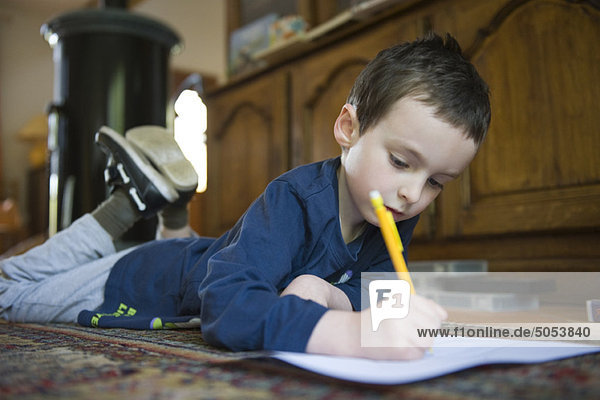 Junge auf dem Boden liegend  Schreiben auf Papier mit Bleistift