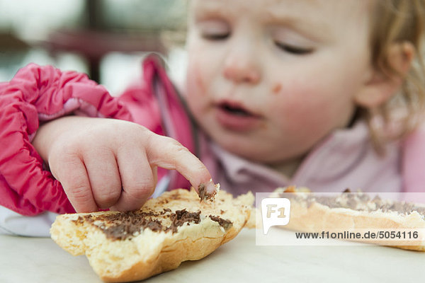 Toddler girl eating baguette with chocolate spread