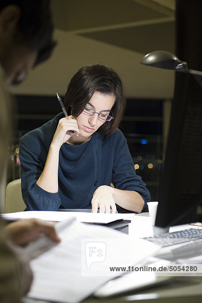 Kollegen beim Lesen von Dokumenten im Büro bei Nacht