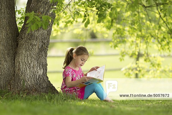 Younge girl reading a book under a tree in Northern Alberta  Canada.